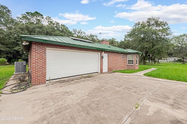 exterior space featuring brick siding, a yard, central air condition unit, concrete driveway, and metal roof