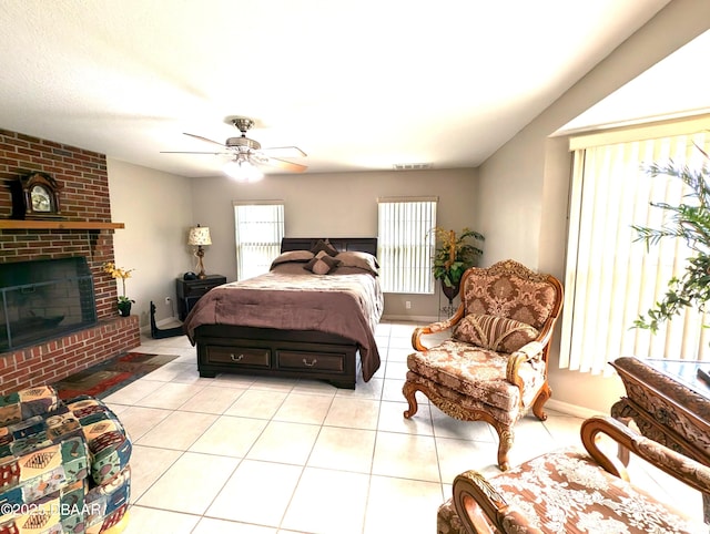 bedroom with a brick fireplace, visible vents, a ceiling fan, and light tile patterned flooring