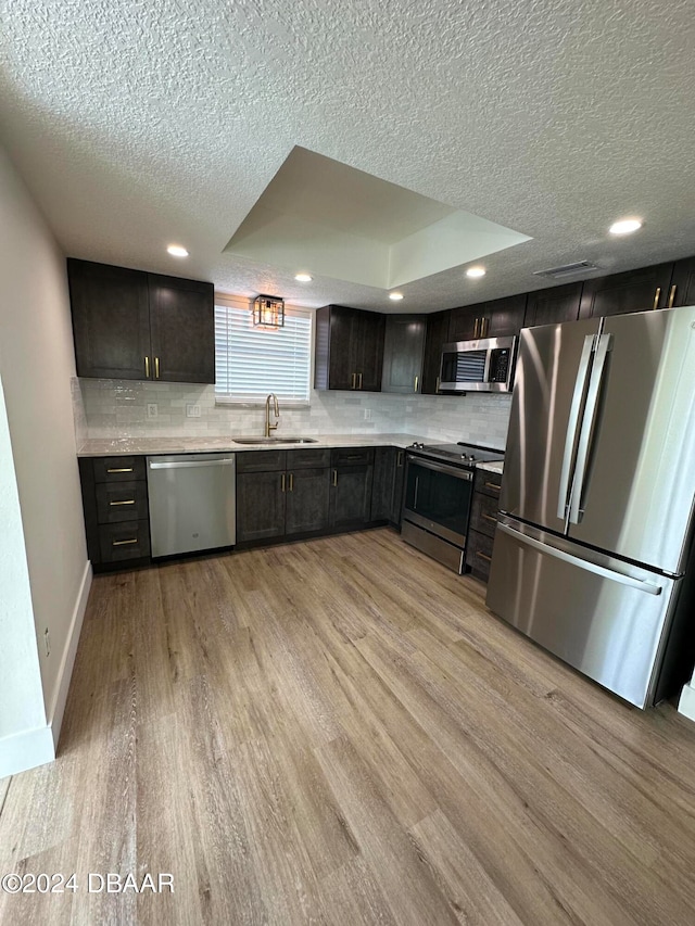 kitchen with light wood-type flooring, appliances with stainless steel finishes, sink, and a raised ceiling