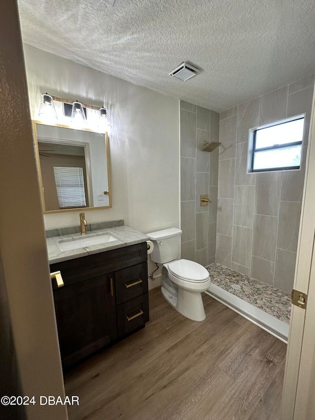 bathroom with hardwood / wood-style floors, a tile shower, and a textured ceiling