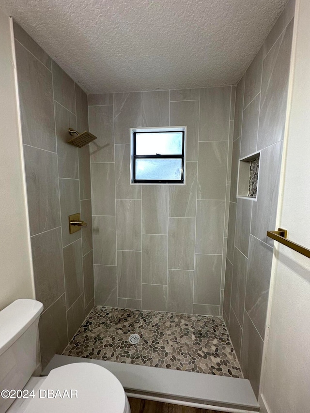 bathroom featuring toilet, a textured ceiling, and tiled shower