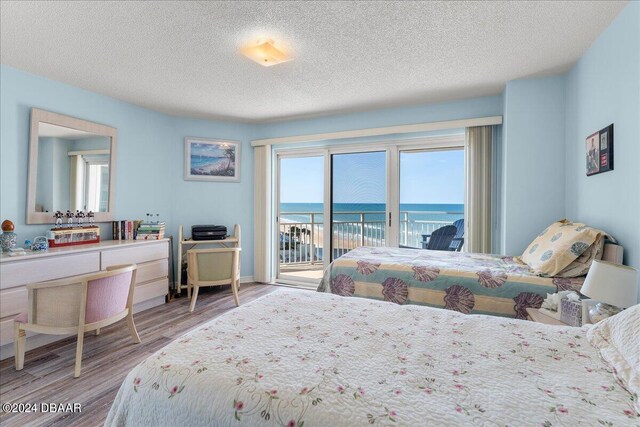 bedroom featuring light hardwood / wood-style floors, multiple windows, a water view, and access to outside
