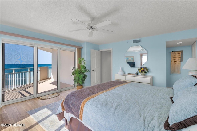 bedroom with a water view, ceiling fan, access to exterior, a textured ceiling, and light hardwood / wood-style flooring
