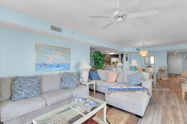 living room with hardwood / wood-style floors, ceiling fan with notable chandelier, and a textured ceiling