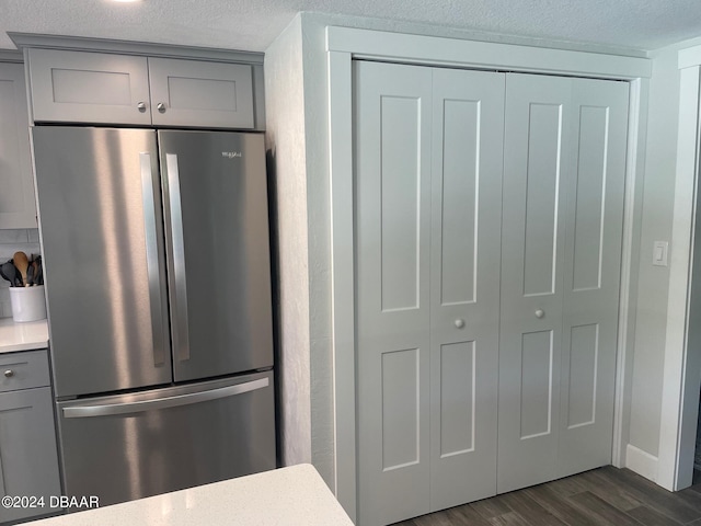 kitchen with gray cabinetry, dark wood-type flooring, stainless steel fridge, and a textured ceiling