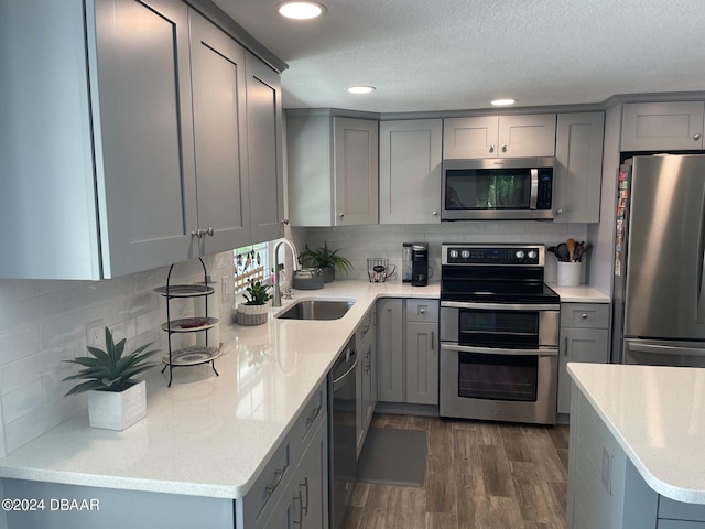 kitchen featuring sink, gray cabinetry, dark hardwood / wood-style flooring, stainless steel appliances, and backsplash