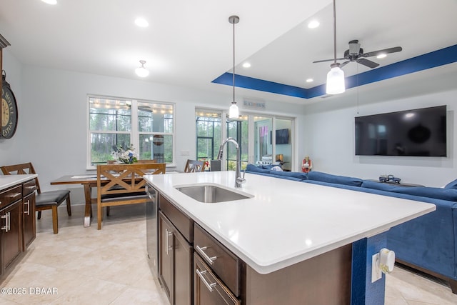 kitchen featuring pendant lighting, a center island with sink, a tray ceiling, dark brown cabinets, and sink