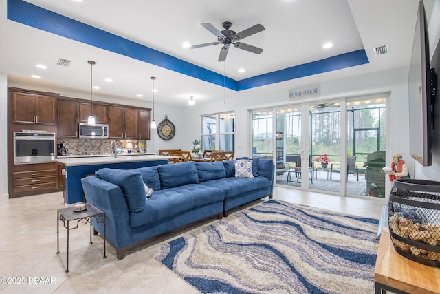 living room featuring light tile patterned floors, ceiling fan, a tray ceiling, and sink