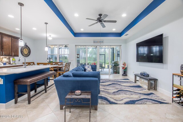 tiled living room featuring ceiling fan, sink, and a tray ceiling