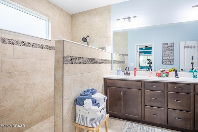 bathroom with a tile shower, tile patterned floors, vanity, and tile walls