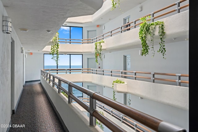 hall with a high ceiling, dark colored carpet, and a water view