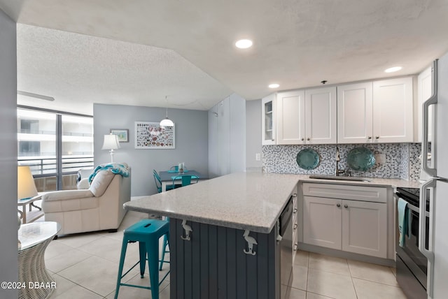 kitchen featuring white cabinetry, sink, kitchen peninsula, a breakfast bar area, and hanging light fixtures