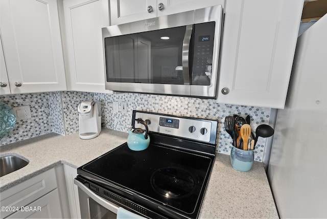 kitchen with backsplash, appliances with stainless steel finishes, light stone countertops, and white cabinets