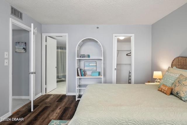 bedroom with dark wood-type flooring, a textured ceiling, a walk in closet, and a closet