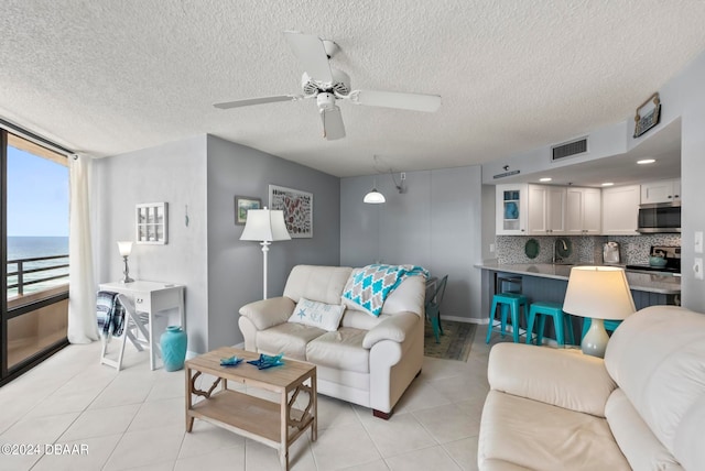 tiled living room with a water view, a textured ceiling, ceiling fan, and sink