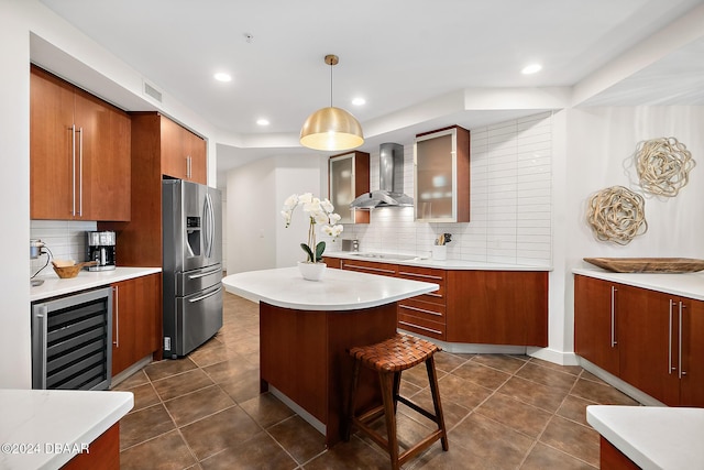 kitchen with beverage cooler, hanging light fixtures, wall chimney range hood, cooktop, and stainless steel fridge