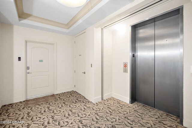 carpeted foyer entrance with elevator and a tray ceiling