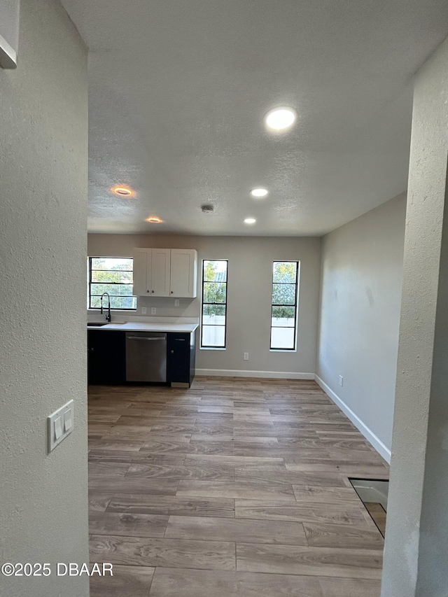 kitchen featuring a textured ceiling, baseboards, light countertops, stainless steel dishwasher, and light wood-type flooring