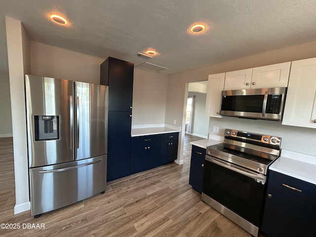 kitchen featuring stainless steel appliances, light countertops, light wood-style floors, white cabinetry, and a textured ceiling