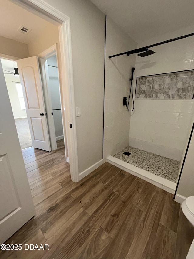 bathroom featuring baseboards, visible vents, a tile shower, and wood finished floors