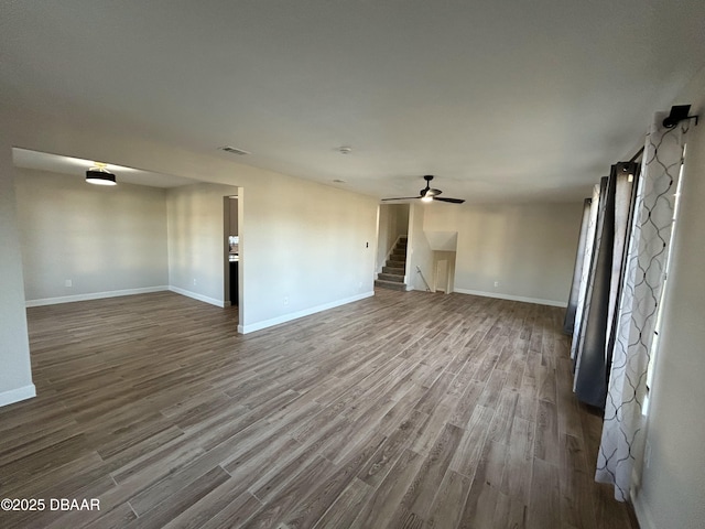 unfurnished living room with a ceiling fan, dark wood-style flooring, baseboards, and stairs