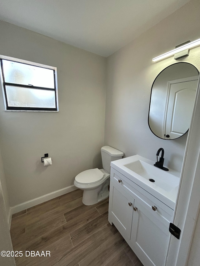 half bath with toilet, baseboards, wood finished floors, and vanity