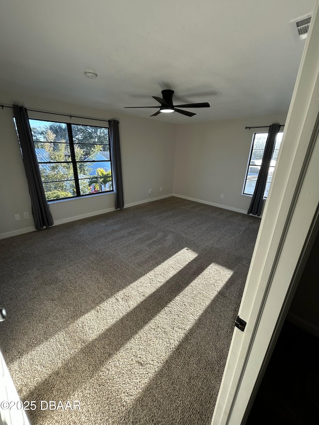 empty room with carpet floors, visible vents, baseboards, and ceiling fan