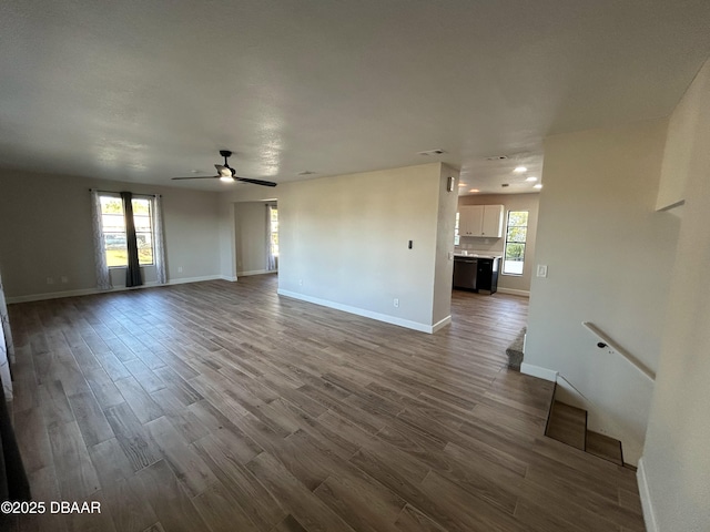 unfurnished living room featuring a healthy amount of sunlight, ceiling fan, baseboards, and wood finished floors