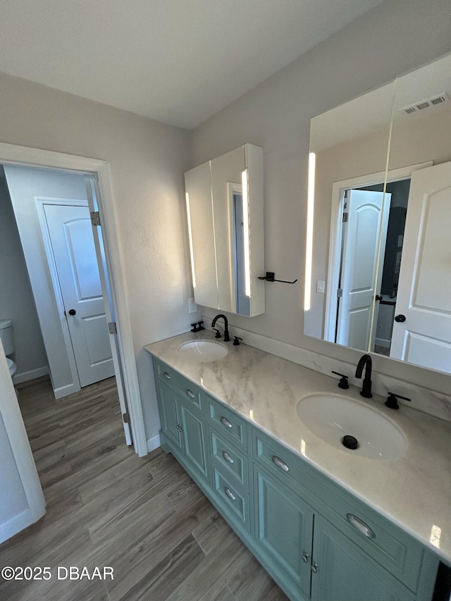 full bath featuring double vanity, visible vents, a sink, and wood finished floors