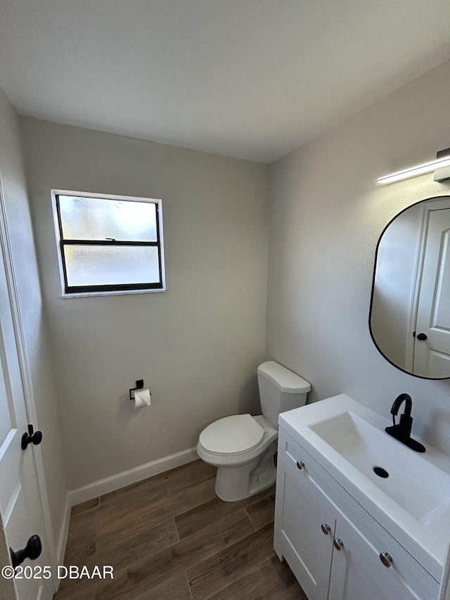 bathroom with toilet, baseboards, wood finished floors, and vanity