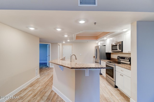 kitchen with a center island with sink, appliances with stainless steel finishes, a breakfast bar area, light hardwood / wood-style flooring, and white cabinets