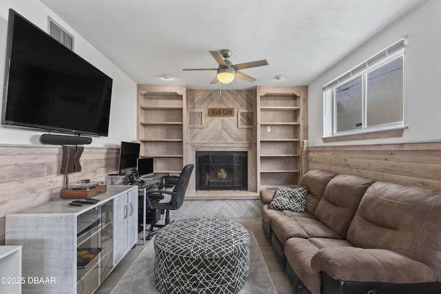 living room with ceiling fan, wood walls, and built in shelves