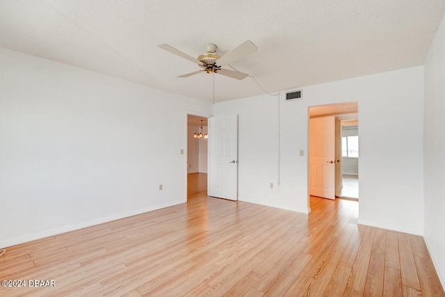 empty room featuring ceiling fan with notable chandelier, a textured ceiling, and light wood-type flooring