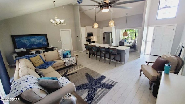 living area with light wood-style floors, high vaulted ceiling, baseboards, and ceiling fan with notable chandelier