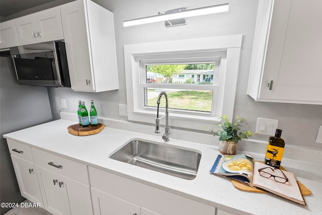 kitchen with white cabinetry, sink, and light stone counters