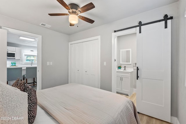 bedroom with ensuite bath, light hardwood / wood-style floors, a barn door, ceiling fan, and a closet