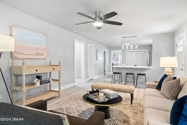 living room with ceiling fan with notable chandelier and light wood-type flooring