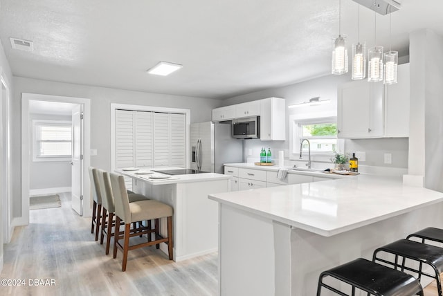 kitchen with stainless steel appliances, light wood-type flooring, white cabinetry, hanging light fixtures, and a breakfast bar