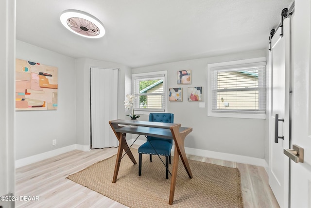 home office with a barn door and light hardwood / wood-style floors