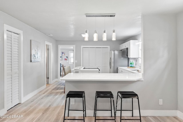 kitchen featuring kitchen peninsula, decorative light fixtures, light hardwood / wood-style floors, and white cabinets