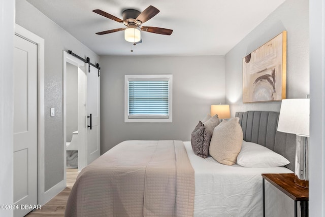 bedroom featuring a barn door, ceiling fan, connected bathroom, and wood-type flooring