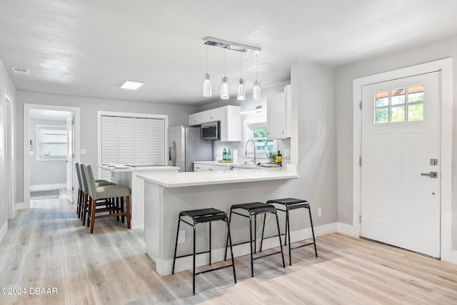 kitchen with stainless steel appliances, white cabinets, kitchen peninsula, hanging light fixtures, and light wood-type flooring