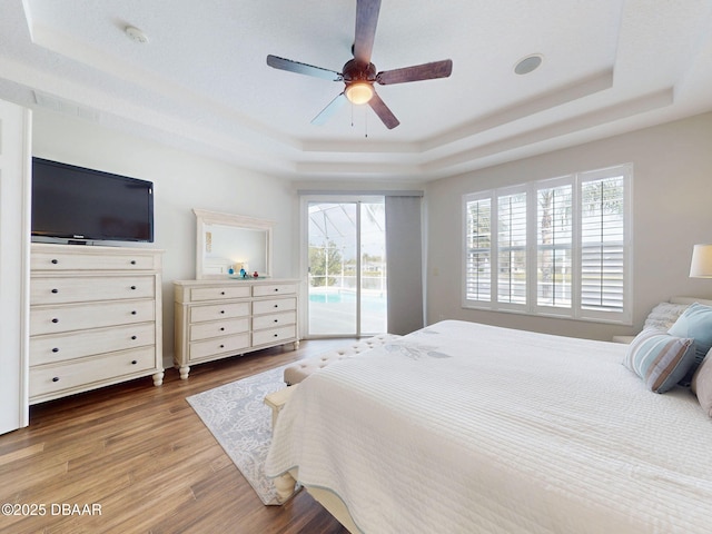 bedroom with access to outside, a ceiling fan, wood finished floors, and a raised ceiling