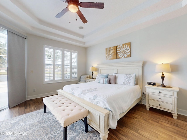 bedroom featuring baseboards, a ceiling fan, a tray ceiling, and wood finished floors