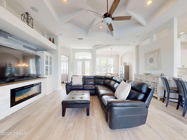 living room featuring a glass covered fireplace, recessed lighting, light wood-style flooring, a ceiling fan, and coffered ceiling