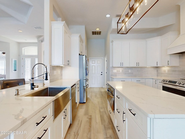 kitchen with visible vents, light wood-type flooring, white cabinets, a sink, and appliances with stainless steel finishes