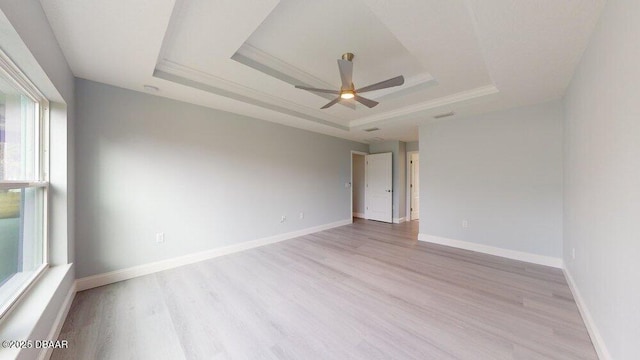 unfurnished room with a raised ceiling, ceiling fan, and light wood-type flooring