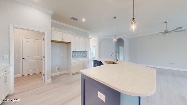 kitchen featuring pendant lighting, sink, a kitchen island with sink, white cabinetry, and tasteful backsplash