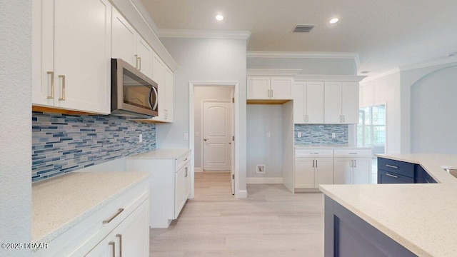 kitchen featuring tasteful backsplash, white cabinetry, ornamental molding, and light wood-type flooring