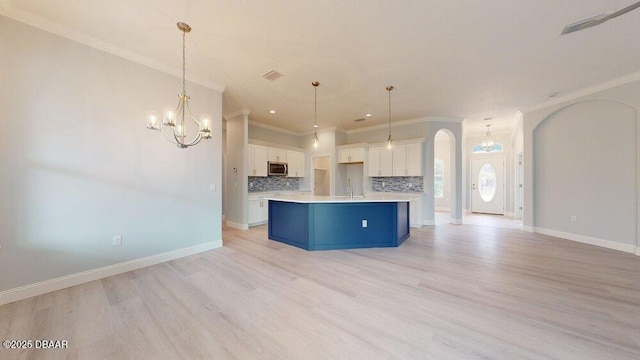 kitchen with white cabinetry, hanging light fixtures, a kitchen island with sink, and tasteful backsplash